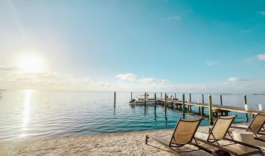 two beach chairs on the beach at sunset with calm water and a dock in the water