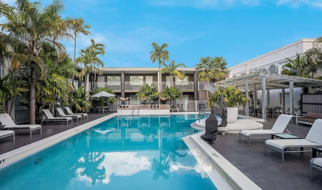 two story motel overlooking pool area with palm trees and pool chairs