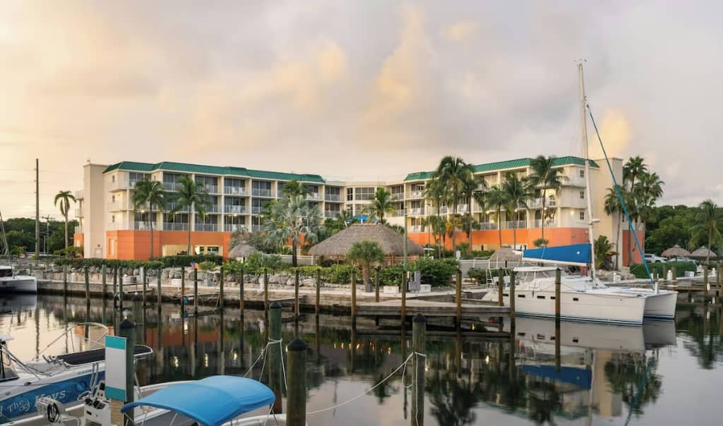 view of 4 story hotel buiding from the water showing several boats docked and a tiki bar at the key largo resort