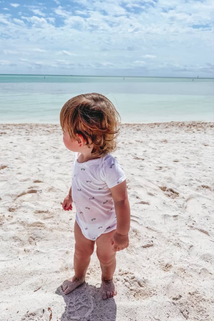 toddler standing on the beach in his onesie on a sunny day